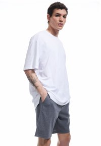 Weißes Baumwoll-T-Shirt mit umgeschlagenen Ärmeln, kombiniert mit grauen strukturierten Shorts, die Seitentaschen und einen lässigen Schnitt bieten.