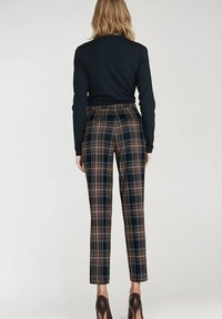 Spodnie w kratę z ciemnym tłem oraz brązowym, niebieskim i pomarańczowym wzorem. Dopasowany krój, prosta nogawka, z średnim stanem.
