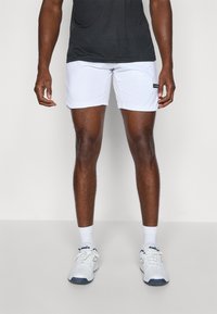 Hvite idrettsshorts laget av lett materiale, med elastisk midjebånd og svart merke på siden, kombinert med hvite joggesko og sokker.