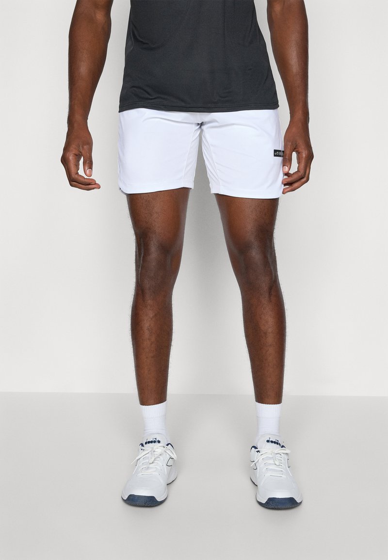 Hvite idrettsshorts laget av lett materiale, med elastisk midjebånd og svart merke på siden, kombinert med hvite joggesko og sokker.