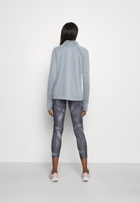 Maglioncino azzurro chiaro a maniche lunghe con colletto, abbinato a leggings scuri attillati con un motivo a vortice. Le scarpe sono di un rosa chiaro.