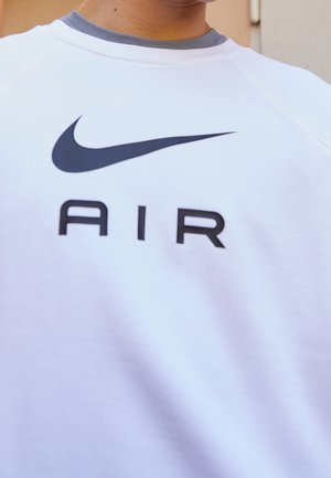 Zbliżenie białej koszuli z czarnym logo Nike swoosh i nadrukowanym pod logo napisem "AIR".