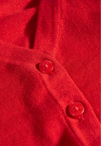 Tissu tricoté rouge avec deux boutons rouges brillants à quatre trous fixés le long d'un bord vertical.