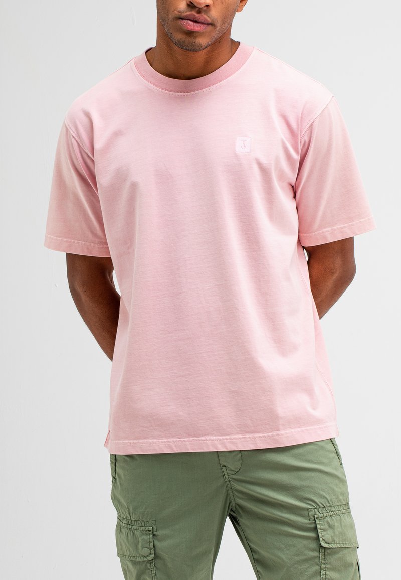 Lichtroze katoenen T-shirt met korte mouwen, ronde hals en een klein logo detail op de linkerborst. Gecombineerd met groene cargobroeken.