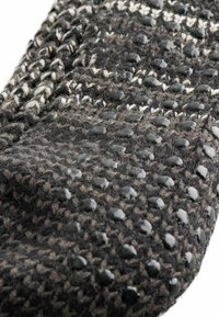 Verstrickter dunkelgrauer und schwarzer Stoff mit einem strukturierten Muster, versehen mit glänzenden schwarzen Gummipunkten, die gleichmäßig für Rutschfestigkeit auf der Oberfläche verteilt sind.