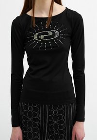 Schwarzes Langarmshirt mit einem kreisförmigen Strassdesign und strahlenförmigen Linien. Weicher Stoff mit einer taillierten Silhouette.