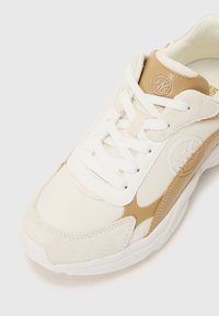 Sneaker atletica bianca e beige con tomaia in rete e suede, dotata di logo rotondo e lacci, suola imbottita e dettagli testurizzati.