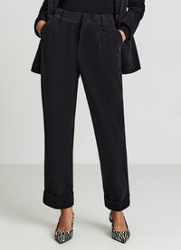 Schwarze Cordhosen mit geradem Bein, vorne mit Falten, Seitentaschen und umgeschlagenen Bündchen, kombiniert mit schwarz-weiß gestreiften High Heels.