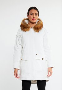 Witte parka met een oranje-bruin faux fur kraag. Heeft twee voorzakken met gouden hardware en een ritsluiting. Glad textuur.