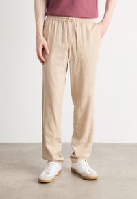 Beige elastiska byxor med dragsko i midjan, rak passform, lätt tyg, kombinerade med vita sneakers med gummisole.