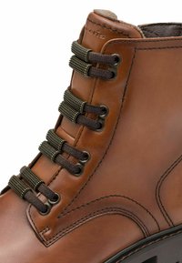 Brązowe skórzane botki za kostkę o teksturowanym wykończeniu, sześcioma oczkami i dopasowanymi sznurówkami. Posiadają wyściełany kołnierz i kontrastowe detale przeszycia.