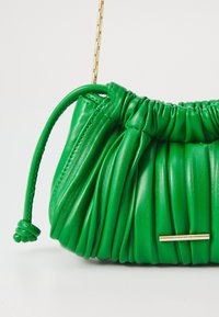 Green leather handbag with pleated design, a gold-tone hardware accent, and a drawstring closure. Features a chain strap for versatility.