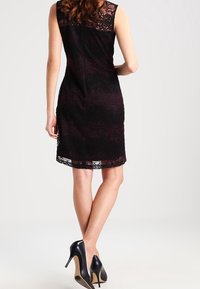 Ärmlös svart spetsklänning med burgunderfärgad underklädsel, knälång, figurnära design, med ett subtilt blommönster och en mjuk textur.