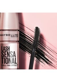 Mascara Maybelline Lash Sensational in un flacone metallico rosa, con un applicatore a setole nere accanto e un design a strisce nere sullo sfondo.