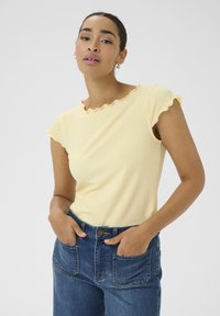 T-shirt jaune à côtes avec un col ondulé et des manches courtes, associé à un jean en denim bleu taille haute avec des poches avant.