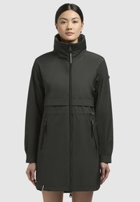 Jachetă impermeabilă de culoare verde închis, cu guler înalt, fermoar frontal, talie elastă și buzunare laterale. Material neted, mat, cu design până la genunchi.