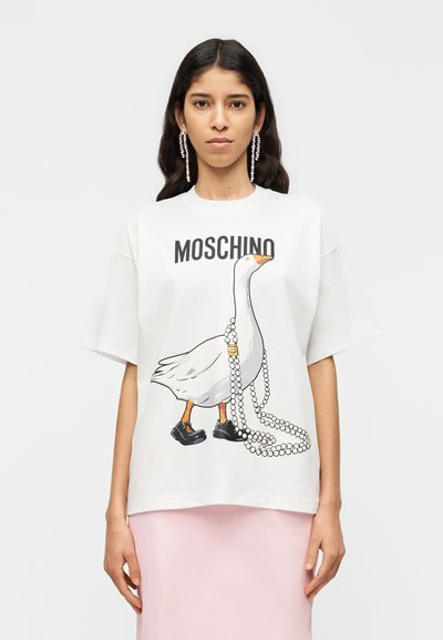 Λευκό βαμβακερό t-shirt με ένα παιχνιδιάρικο γραφικό πάπιας με μαύρα παπούτσια που κρατάει ένα νήμα από μαργαριτάρια. Το όνομα της μάρκας "MOSCHINO" είναι τυπωμένο από πάνω.