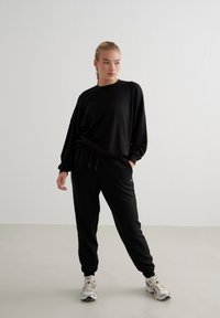 Schwarzer Baumwollmischungs-Sweatshirt mit überschnittenen Schultern, lockerer Passform und passenden tapered Jogginghosen. Ausgestattet mit dezentem Branding und elastischen Bündchen.