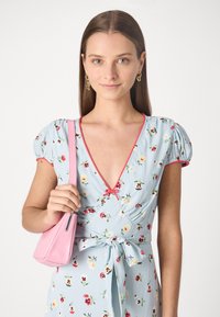 Rochie florala de culoare albastru deschis, cu maneci bufante, accente rosii si un cordon la talie. Modelul tine o geanta mica roz, cu un finisaj texturat.