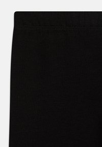 Čierne bavlnené legíny s hladkým povrchom a elastickým pásom. Materiál vyzerá pružne a vytvára priliehavý strih.