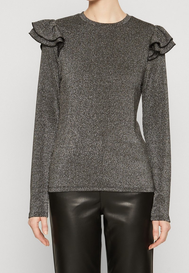 Top lungo nero a maniche lunghe realizzato in tessuto tessuto metallico testurizzato; presenta dettagli arricciati sulle spalle e un colletto tondo. Indossato con pantaloni neri.