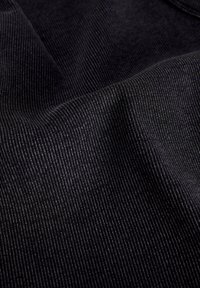 Gros plan de tissu en velours côtelé noir avec de fines côtes verticales et des plis doux créant texture et profondeur.