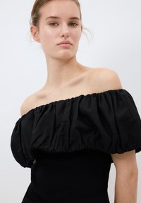 Top nero scollato con design a maniche a sbuffo arricciate e texture a coste sul corpo aderente. Finitura in tessuto liscia.
