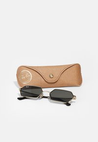 Ray-Ban aurinkolasit, joissa on oktaalinen muoto, mustat linssit, kultainen metallinen kehys ja mustat templet. Mukana vaaleanruskea teksturoitu kotelo.