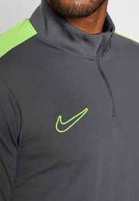 Nike grijze performance quarter-zip top met een gestructureerde groene accent op de schouders en een felgroen geborduurd logo.
