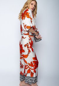 Długi, biały szlafrok z żywymi pomarańczowymi wzorami kwiatowymi. Posiada zwężoną talię oraz czarne dekoracyjne wykończenie przy mankietach i hemie.