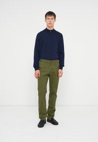 Granatowy pulower z zamkiem na szyi, zielone bawełniane spodnie stretch i czarne buty wsuwane. Minimalistyczny design z dopasowanym krojem i teksturowanym materiałem.