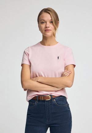 Roze t-shirt met korte mouwen van katoen, met een klein zwart logo aan de linkerkant. Gepaarde met donkerblauwe high-waist jeans en een bruine riem.
