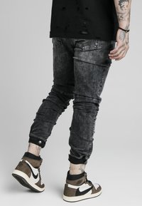 Vaqueros de denim negros ajustados, desgastados y con detalles rasgados, con dobladillos remangados, combinados con zapatillas altas marrones con acentos blancos.