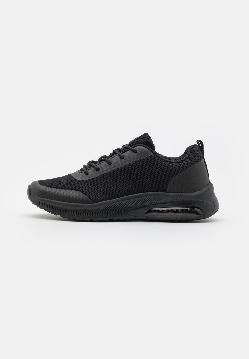 Baskets de sport noires avec tige en mesh, fermeture à lacets sur le devant, semelle rembourrée et coussin d'air visible au talon, présentées de profil sur fond blanc.