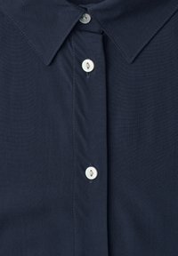 Dark blue shirt with pointed collar and three visible small white buttons down the front center.
