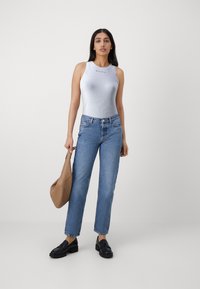 Canotta bianca a coste con logo, jeans a gamba dritta blu chiaro, mocassini neri e una borsa a secchiello color beige. Texture lisce e design aderente.