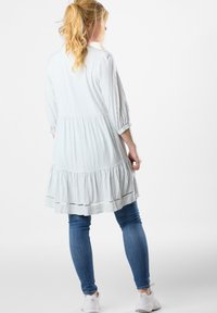 Gestreiftes Kleid in Hellblau und Weiß, mit einem gestuften Rüschensaum, Dreiviertelärmeln und einer lockeren Passform. Kombiniert mit Jeans.