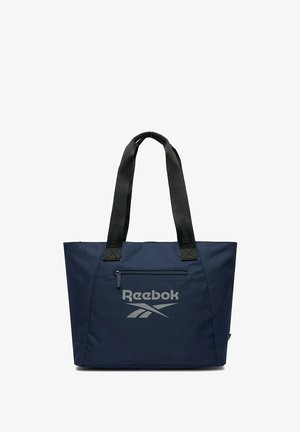 Granatowa torba typu tote Reebok z czarnymi uchwytami, przednią kieszenią na zamek oraz logo Reebok w kolorze szarym nadrukowanym z przodu.