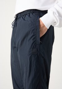 Tumši zili viegli jogger bikses ar elastīgu jostasvītru, aukliņu, sānu kabatām un teksturētu audumu. Iezīmēts ar mazu melnu BOSS logo.