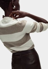 Sweter w paski w kolorze kremowym i taupe, z okrągłym dekoltem i teksturą dzianiny, zestawiony z ciemną skórzaną spódnicą z detalem zamka.