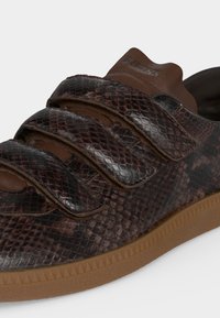 Baskets marron foncé à texture peau de serpent avec trois bandes velcro sur une semelle marron clair.