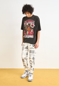 Camiseta gráfica negra con la imagen de Michael Jordan, combinada con pantalones jogger blancos con un patrón y zapatillas gris claro con acentos oscuros.