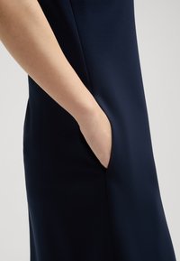 Marineblauwe jurk met een gladde, matte textuur, met een zijzak die is geïntegreerd in de naad voor een gestroomlijnd ontwerp.