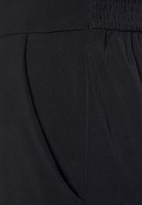 Zwarte, elastische broek met een gladde textuur, voorzien van een gerimpelde tailleband en zijzak. Minimalistisch ontwerp zonder patronen of accenten.
