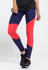 Puma träningsleggings med en blå och röd färgblockdesign, slät yta och en åtsittande form. Kombineras med svarta träningsskor.