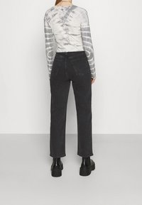 Jeans negros de pierna recta hechos de mezclilla, con una cintura alta, dos bolsillos traseros y una textura suave. Combinados con una camiseta de manga larga de teñido anudado en gris.