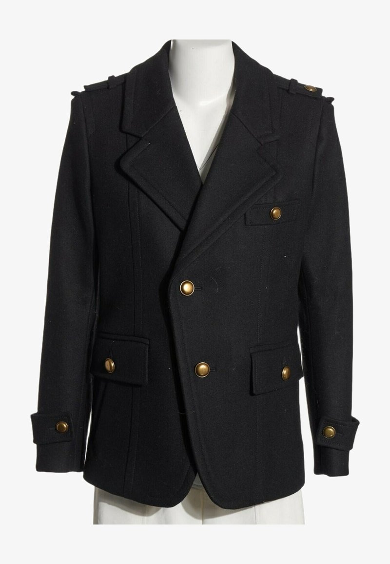 Manteau pea coat noir croisé avec boutons dorés, col cranté, épaulettes et poches à rabat sur un torse de mannequin blanc.