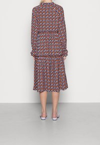 Vestido floral de manga larga; patrones en púrpura, naranja y blanco sobre un fondo oscuro; dobladillo con volantes; puños elásticos; combinado con sandalias ligeras.