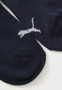 Calzini lavorati a maglia blu navy con un logo di un gatto che salta in bianco sulla parte superiore, fotografati su uno sfondo bianco.