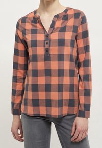 Långärmad orange och marinblå rutskjorta med knäppning och rundad halsringning. Tillverkad av lättviktig tyg och har en avslappnad passform.